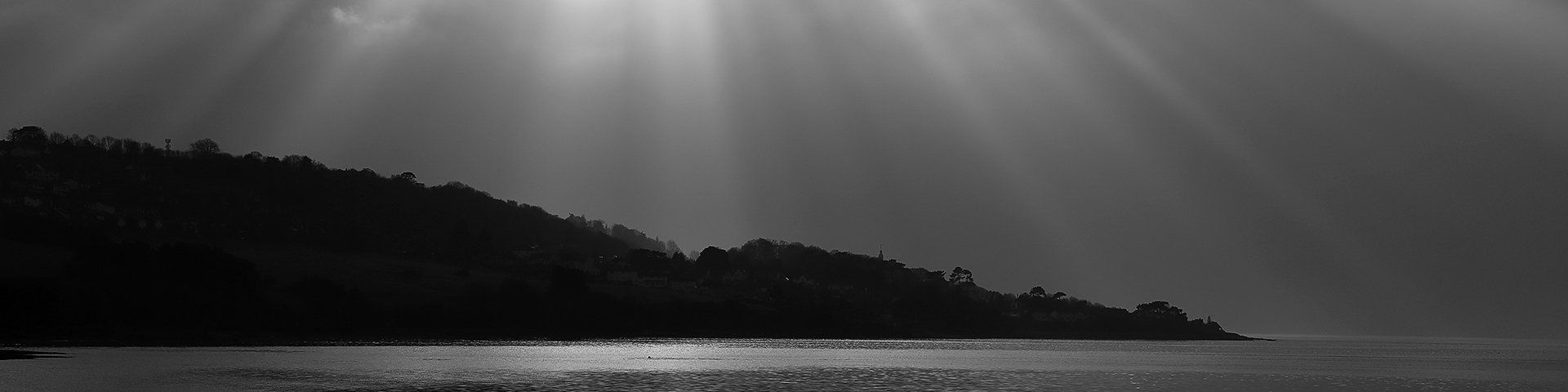 A black and white picture of a coastline with a burst of sunlight above.